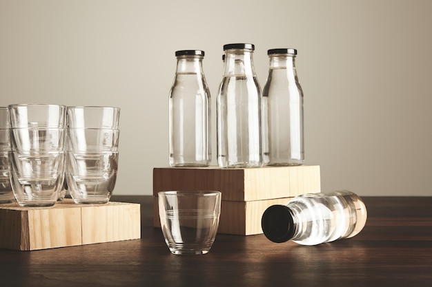 Perfect set of pure clean healthy water in transparent glass bottles and cups presented on wooden