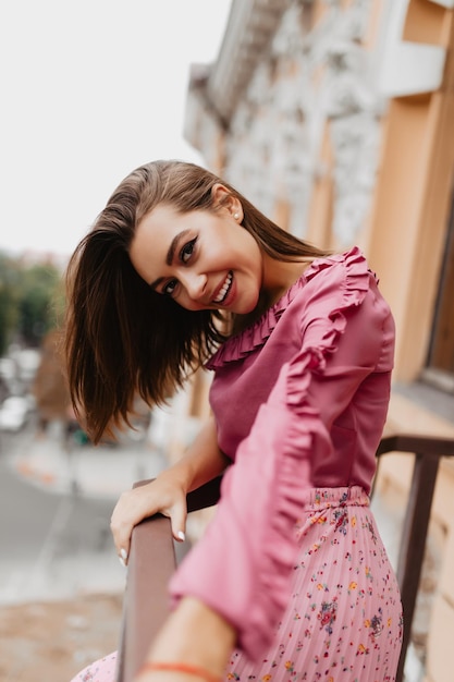 Free photo perky woman in soft tender blouse looks at camera coquettishly portrait of stylish european woman stretching towards camera on balcony