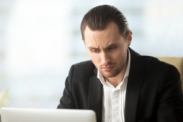 Perplexed young businessman looking at laptop screen 