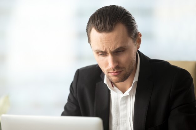 Perplexed young businessman looking at laptop screen 