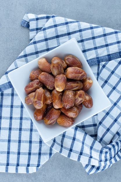 Datteri persiani nella ciotola, sullo strofinaccio, sul tavolo di marmo.