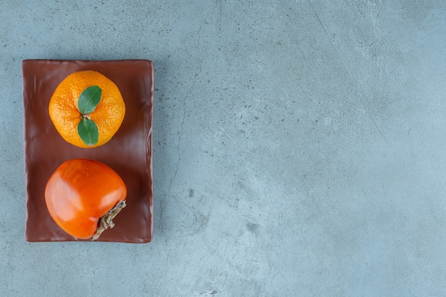 Cachi e arancia sul piatto di legno, sullo sfondo di marmo. foto di alta qualità
