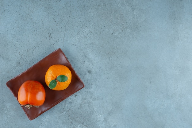 Persimmon and orange on the wooden plate , on the marble table. 