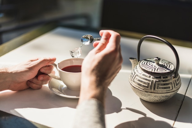 A person adding ice cube in the red tea cup