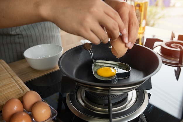 Person breaking an egg into heart mold in a pan