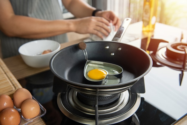 Person breaking an egg into heart mold in a pan