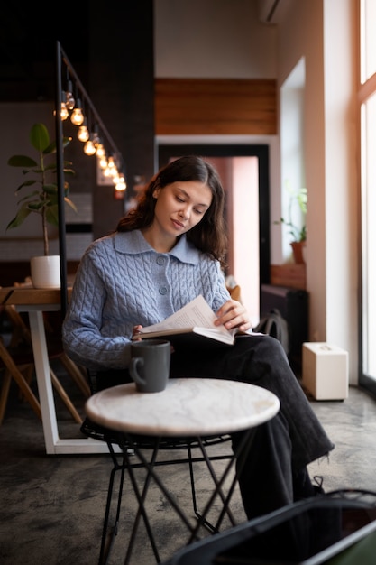 Foto gratuita persona in un bar che legge un libro mentre beve un caffè