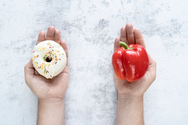 Person choosing between bellpepper and donut over textured background