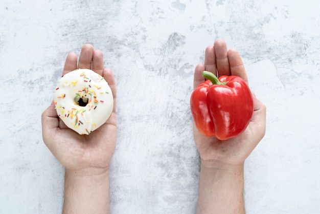 Person choosing between bellpepper and donut over textured background