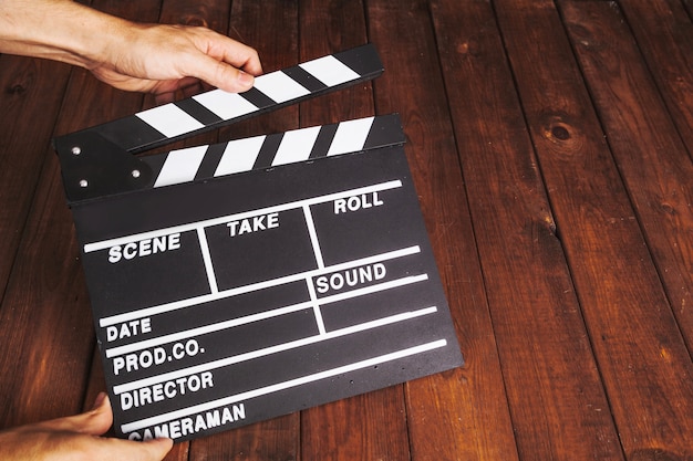 Человек хлопает clapperboard над деревянной столешницей