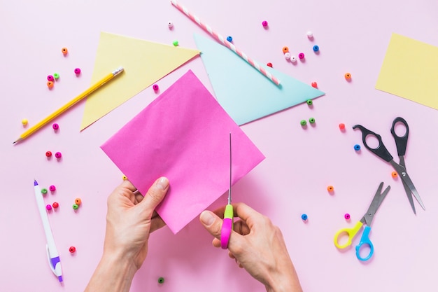 Free photo a person cutting paper with scissor over the pink backdrop