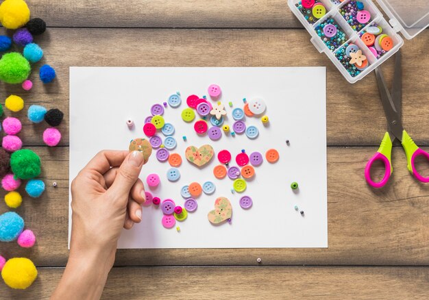 A person decorating white paper with colorful buttons over wooden table
