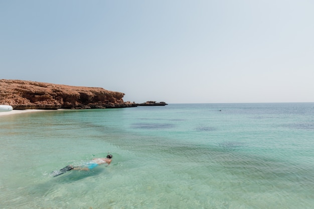 Person diving in the sea near the rocky cliffs under the clear blue sky