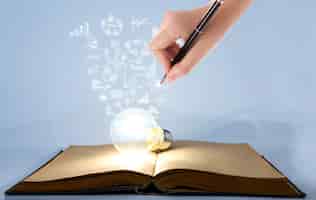 Free photo person drawing symbols coming out of a light bulb on top of a book