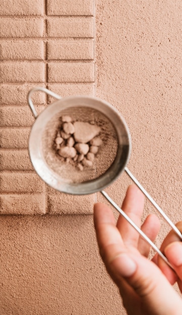 Foto gratuita una persona che spolvera la polvere di cacao dal setaccio sulla tavoletta di cioccolato