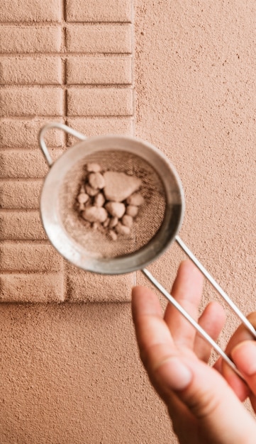 A person dusting cocoa powder from sieve on chocolate bar