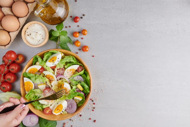 Person eating healthy salad of fresh vegetables and boiled eggs