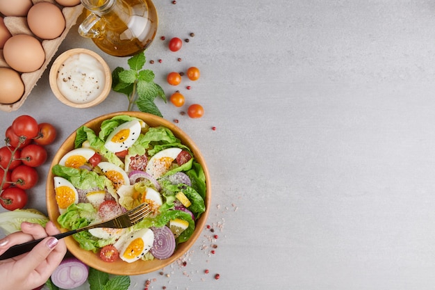 Person eating healthy salad of fresh vegetables and boiled eggs