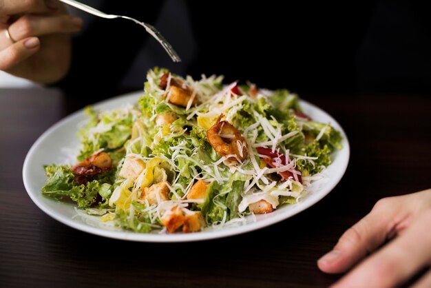 Person eating tasty caesar salad with croutons in restaurant