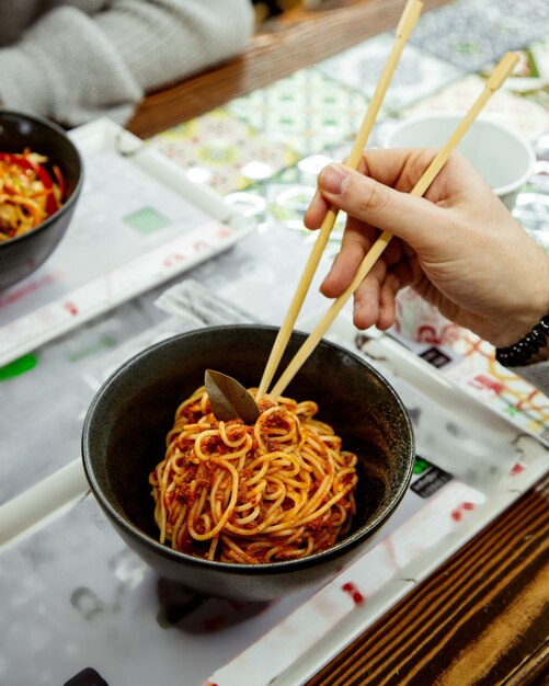 A person eating tomato spaghetti with sticks