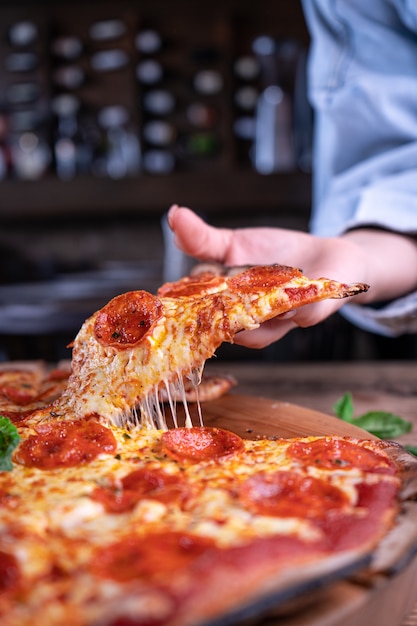 person getting a piece of delicious cheesy pepperoni pizza