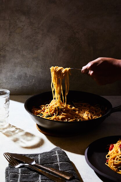 человек получает немного спагетти из черного горшка на белом столе