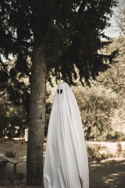 Person in ghost costume standing near tree