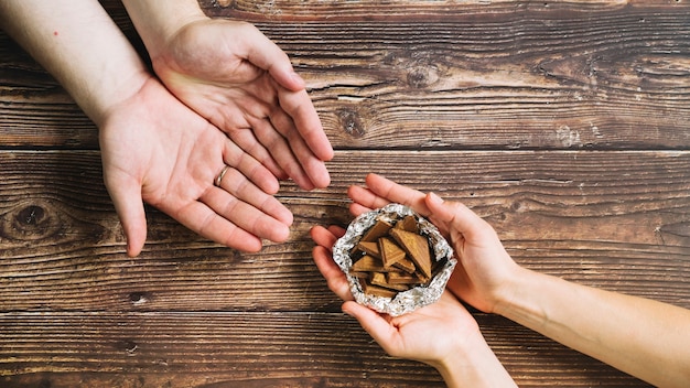 A person giving chocolate pieces in the foil on wooden backdrop