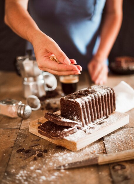 A person giving walnut toppings over the slice of cake on chopping board