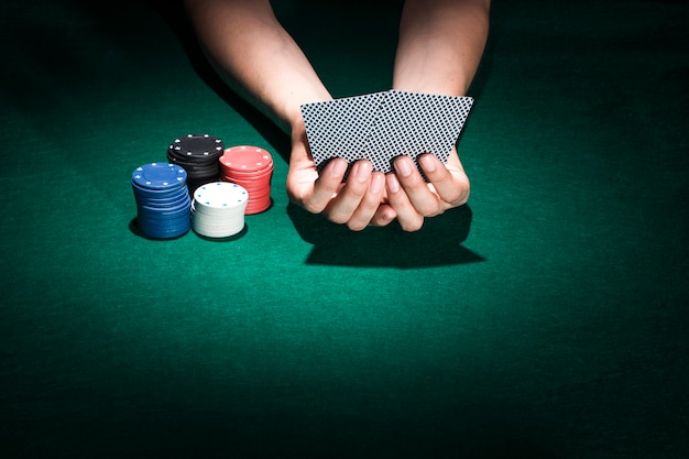 Foto gratuita una carta da gioco della tenuta della mano della persona con l'impilamento dei chip di poker sulla tavola del casinò