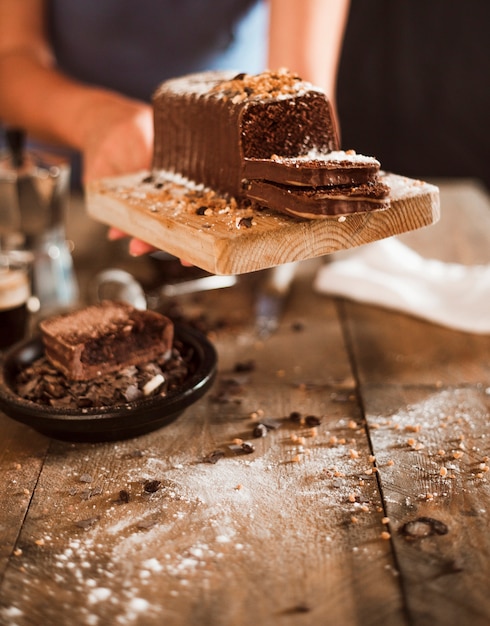 A person hand holding slice of cake on chopping board