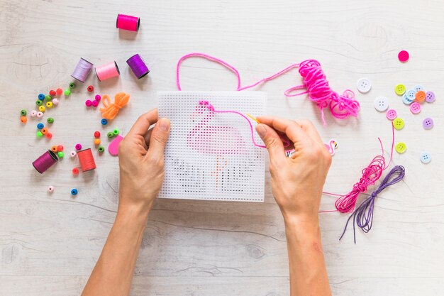 A person hand's doing embroidery with decorative elements on textured backdrop