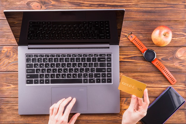 Person hand using gold card for online shopping with laptop over wooden table