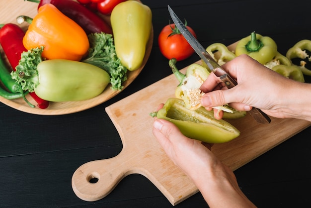 Foto gratuita una mano della persona con il coltello che tiene il peperone sul bancone nero della cucina