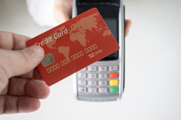 Бесплатное фото Человек, держащий красную кредитную карту с размытым платежным терминалом на заднем плане