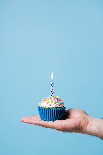 Person holding birthday cupcake with candle 