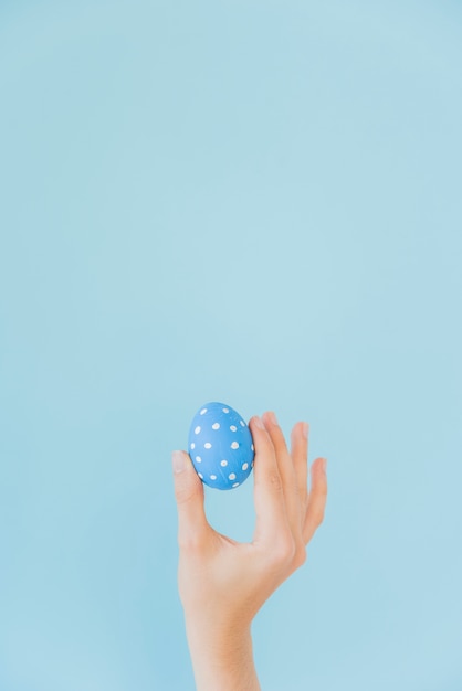 Лицо, занимающее синее пасхальное яйцо в руке