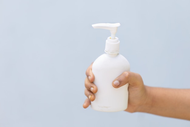 Person holding a bottle of hand press sanitizer with a grey wall