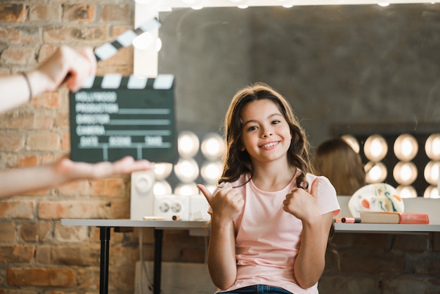 Free photo a person holding clapper board in front of girl showing thumb up sign