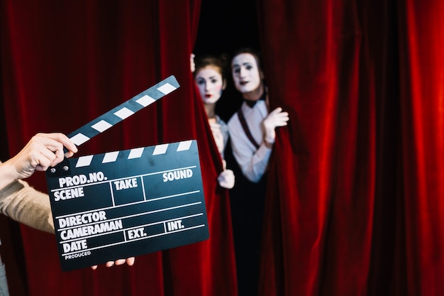 A person holding clapperboard in front of mime couple standing behind the red curtain