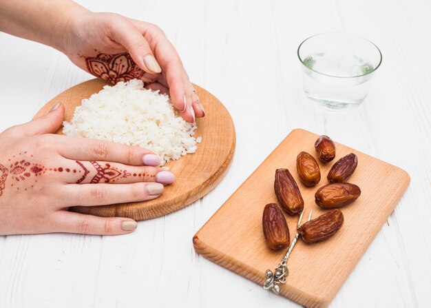 Person holding cooked rice on board near dates fruit 