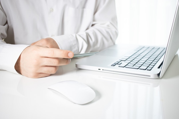 Человек, держащий кредитную карту с ноутбуком и компьютерной мышью на белом столе