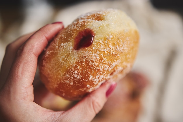 Foto gratuita persona in possesso di una soffice ciambella piena di marmellata sotto le luci con uno sfondo sfocato