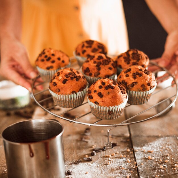 A person holding fresh baked muffins on cooling tray