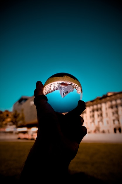 A person holding a glass ball with the reflection of buildings and the blue sky