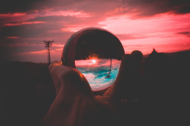 Человек держит стеклянный шар с отражением красочного неба и красивого заката