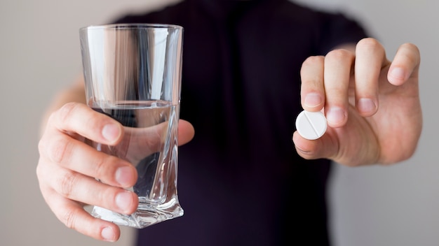 Person holding glass of water and a pill