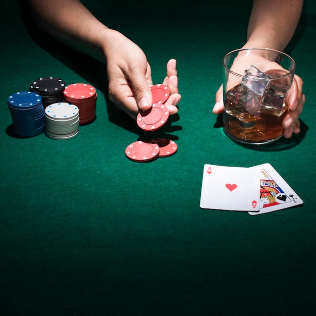 A person holding glass of whiskey while playing poker card