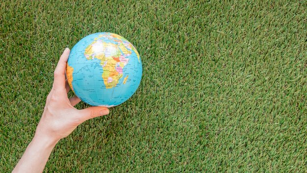 Person holding a globe on grass with copy space