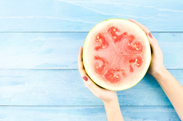 Person holding half of fresh watermelon on table